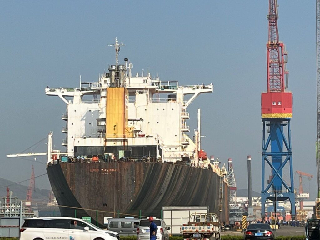 An LNG carrier under conversion at a shipyard quay in China, beside a portal crane