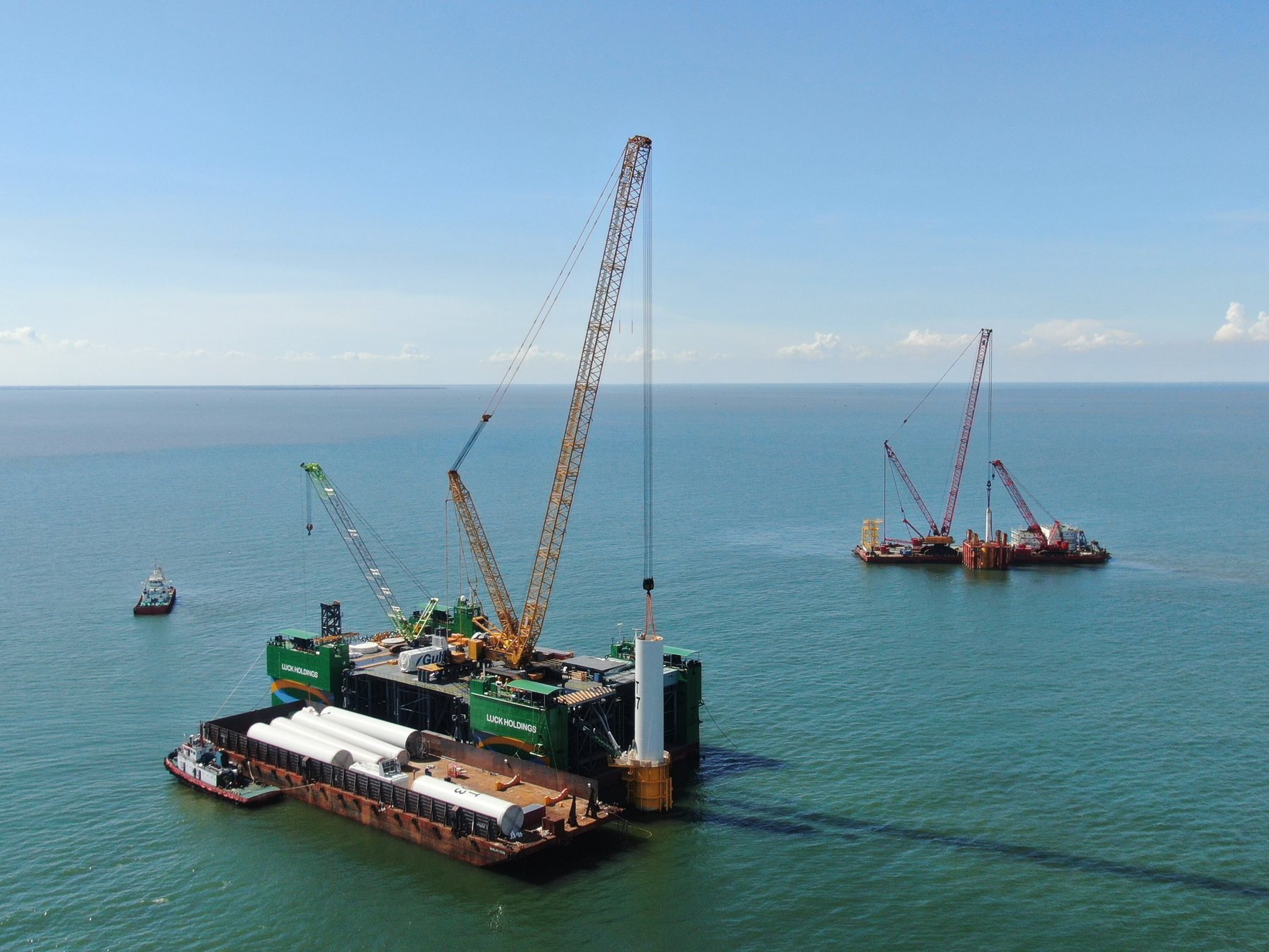 Jack-up crane vessel lifting a wind turbine tower section beside a barge loaded with tower sections, offshore Vietnam