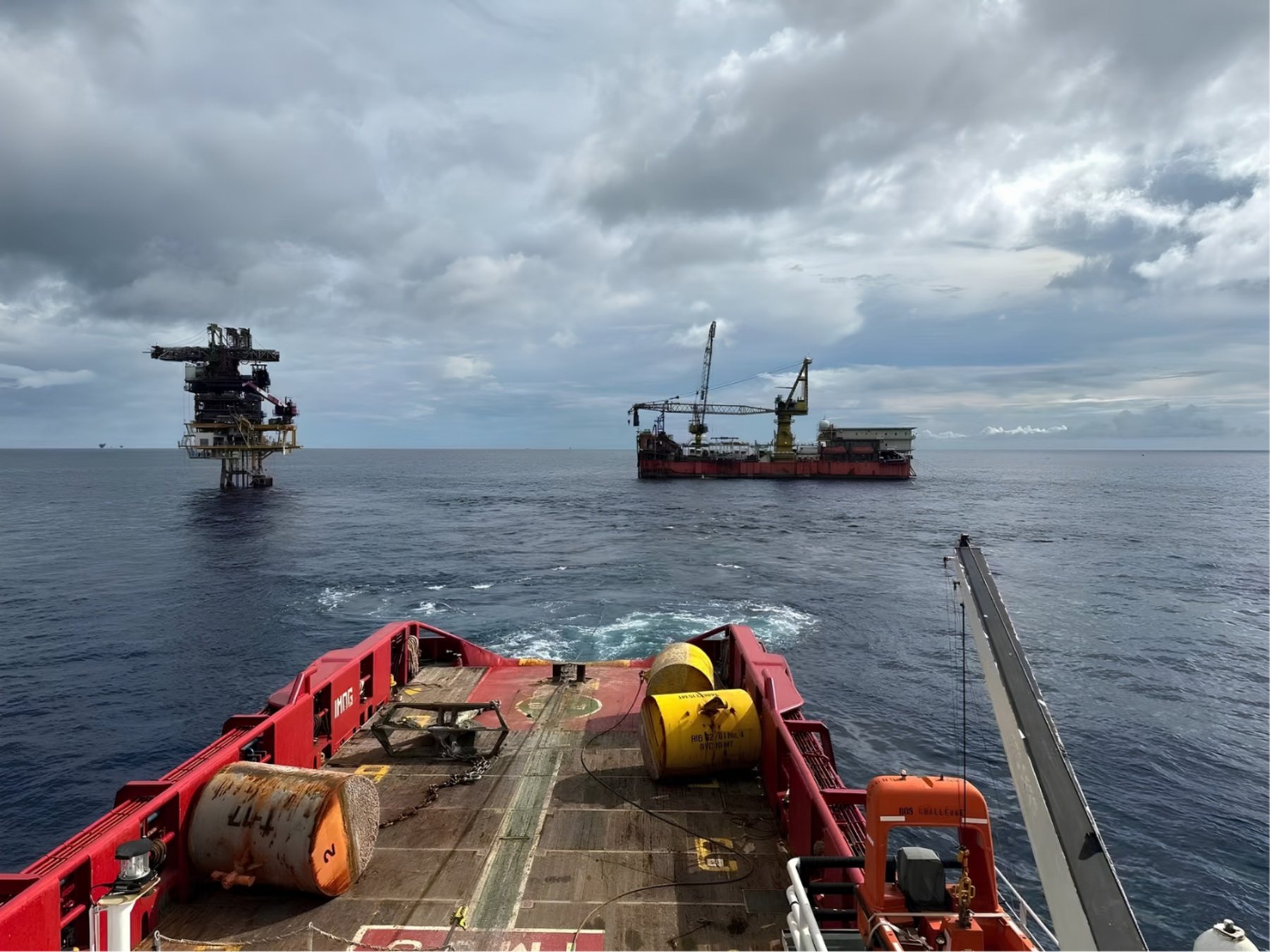View from an anchor handling vessel deck with mooring buoys, towards an offshore platform and a tender rig