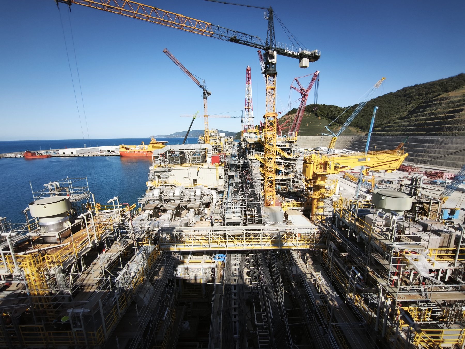 Floating production unit topsides under construction at a shipyard quayside, with tower cranes overhead