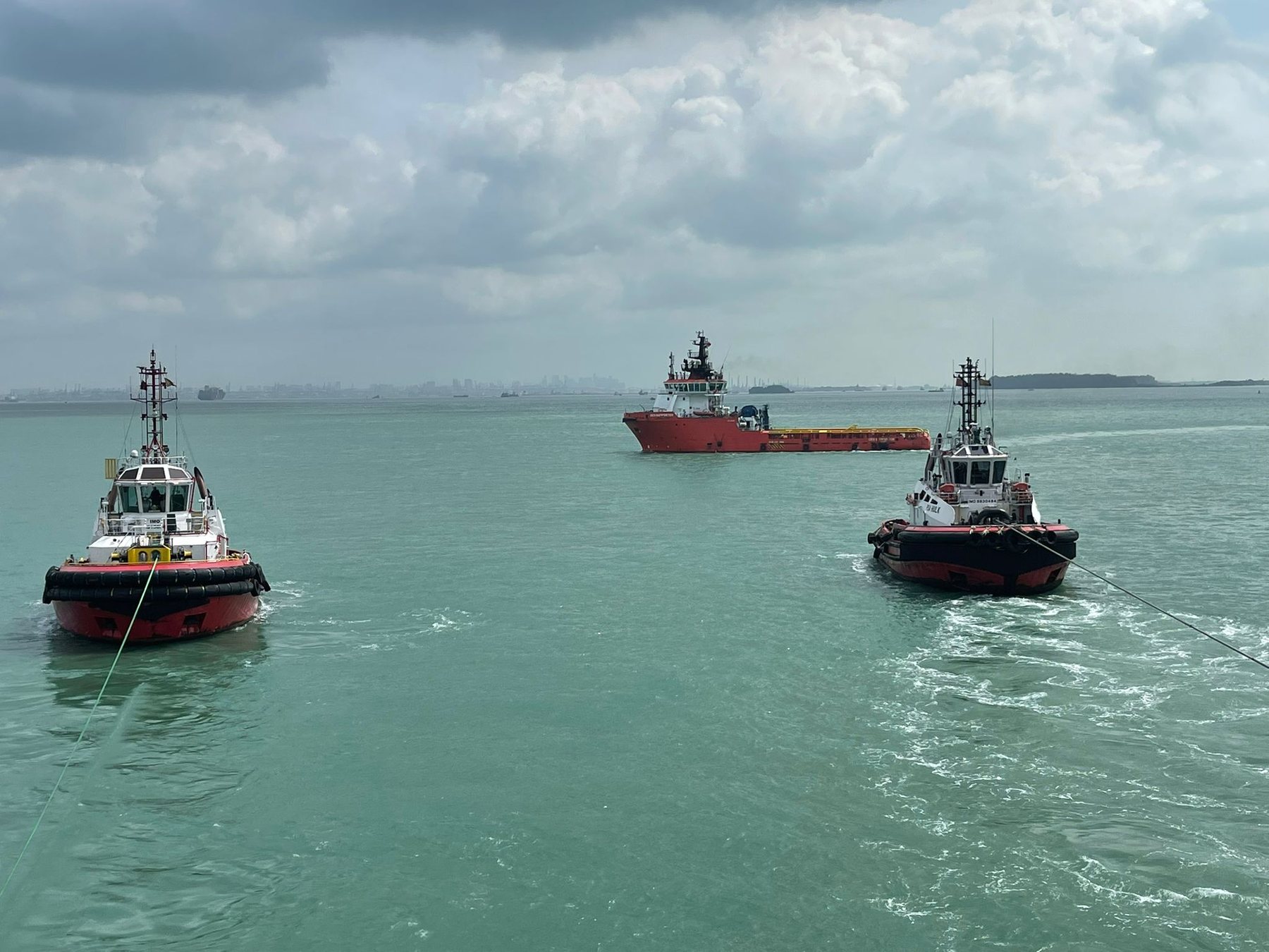 Two tugs towing ahead of an offshore supply vessel in coastal waters