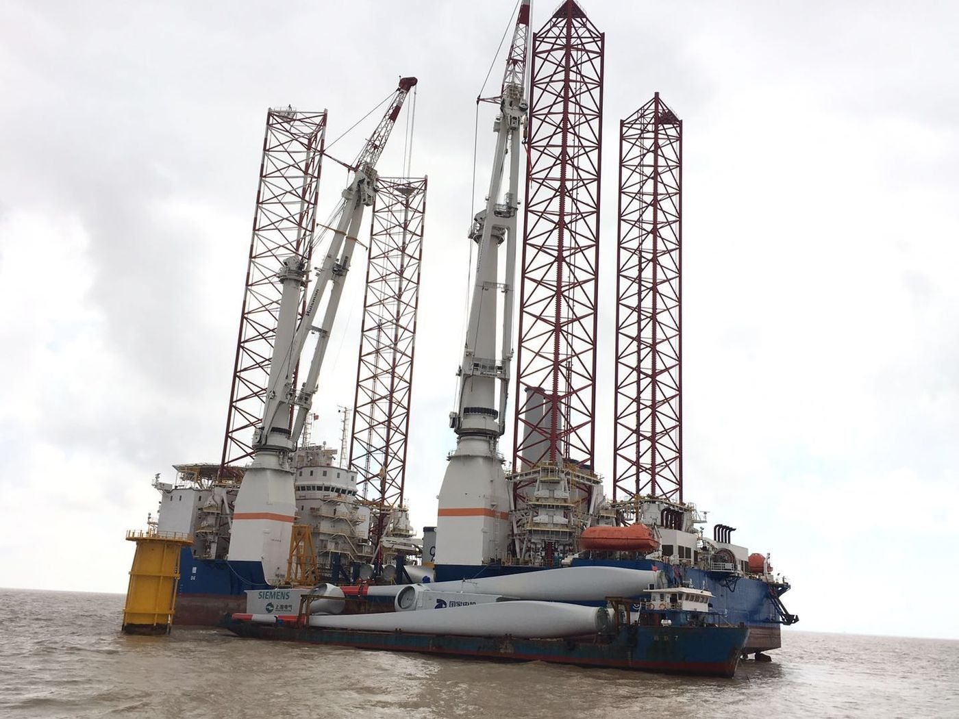 Jack-up wind turbine installation vessel with turbine blades and nacelles on a barge alongside, offshore China